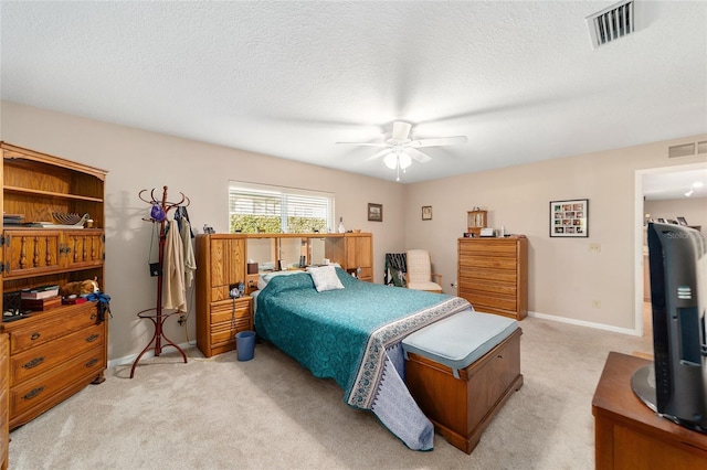 bedroom with ceiling fan, light colored carpet, and a textured ceiling