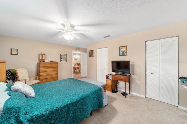 carpeted bedroom featuring ceiling fan, a textured ceiling, and multiple closets