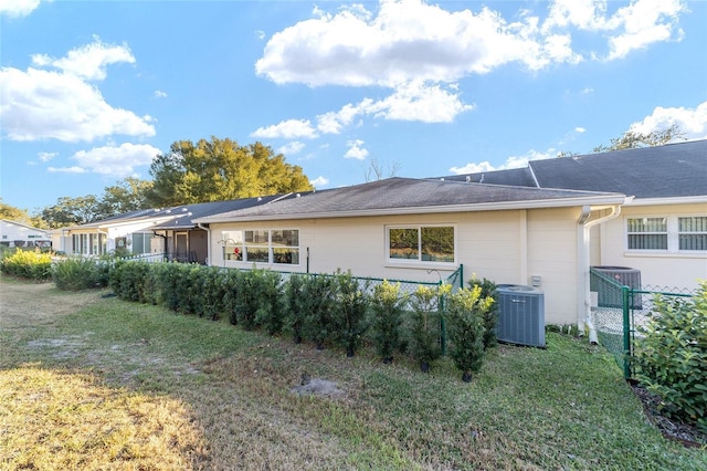 rear view of house with central AC and a lawn