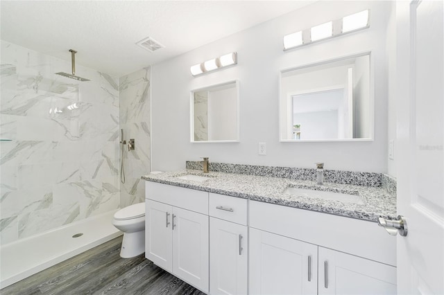 bathroom featuring vanity, hardwood / wood-style flooring, toilet, tiled shower, and a textured ceiling