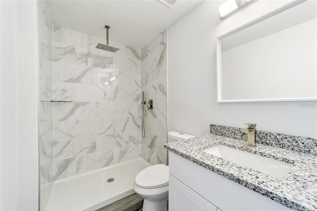 bathroom featuring a tile shower, wood-type flooring, a textured ceiling, toilet, and vanity