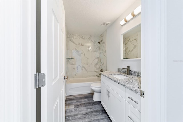 full bathroom with tiled shower / bath combo, hardwood / wood-style floors, a textured ceiling, toilet, and vanity