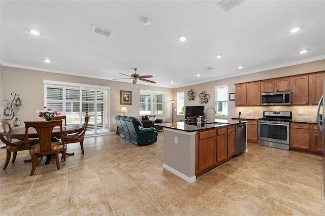 kitchen with ceiling fan, crown molding, an island with sink, and appliances with stainless steel finishes