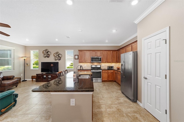 kitchen featuring sink, stainless steel appliances, dark stone countertops, an island with sink, and ornamental molding