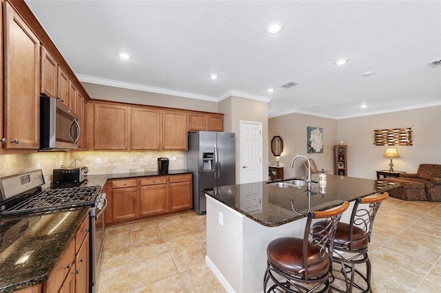 kitchen with crown molding, sink, dark stone countertops, an island with sink, and appliances with stainless steel finishes