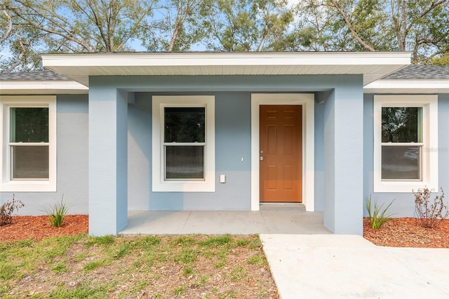 property entrance with a shingled roof and stucco siding