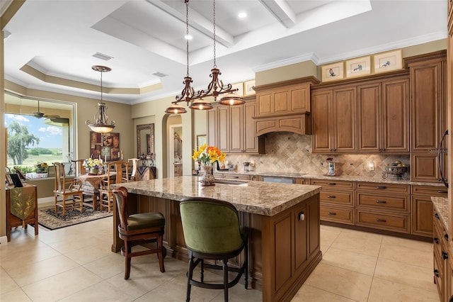 kitchen featuring pendant lighting, a center island with sink, a kitchen breakfast bar, a raised ceiling, and light stone countertops