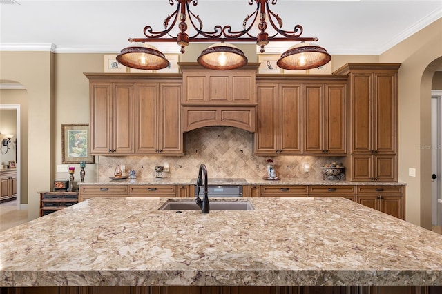 kitchen featuring light stone countertops, backsplash, crown molding, sink, and an island with sink