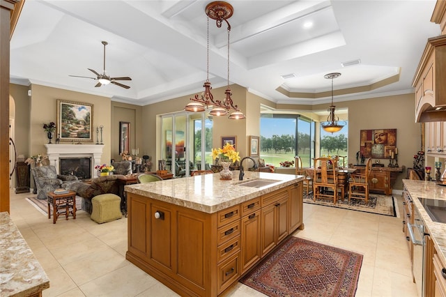 kitchen with decorative light fixtures, ceiling fan with notable chandelier, a tray ceiling, and a kitchen island with sink