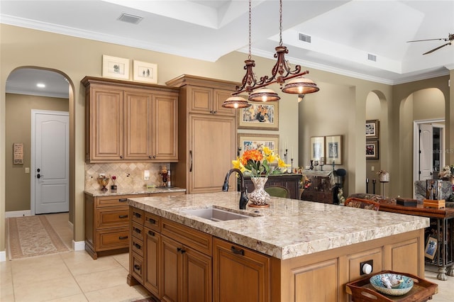 kitchen featuring decorative backsplash, a tray ceiling, a kitchen island with sink, crown molding, and sink