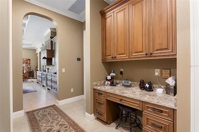 bar with light tile patterned floors, built in desk, light stone counters, and ornamental molding