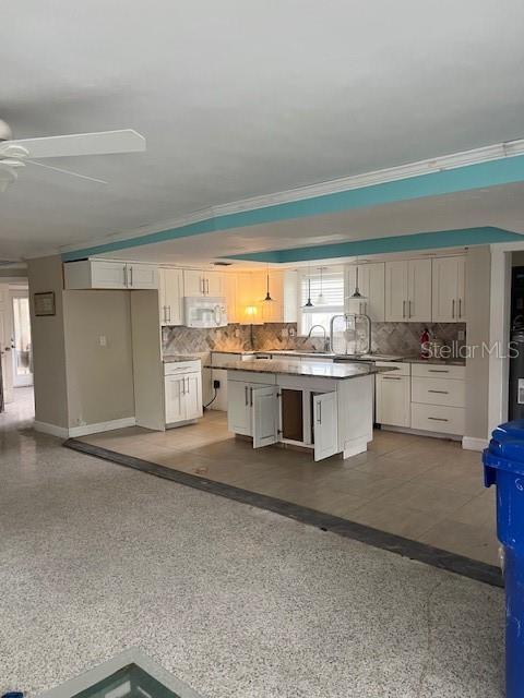 kitchen featuring ceiling fan, white cabinetry, a center island, and crown molding