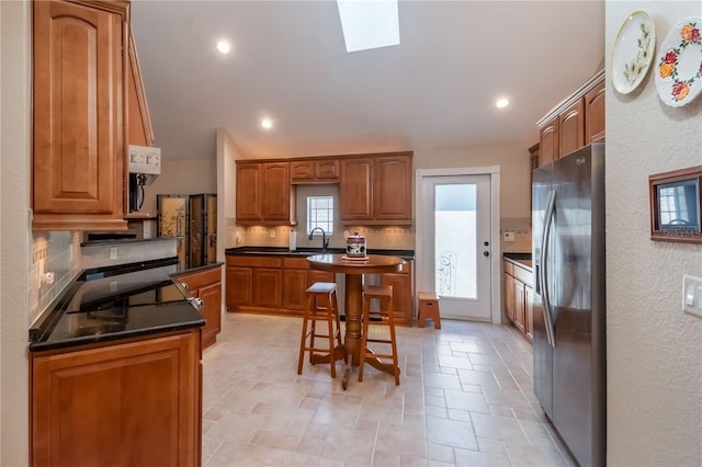 kitchen with sink, a center island, vaulted ceiling with skylight, stainless steel refrigerator with ice dispenser, and decorative backsplash