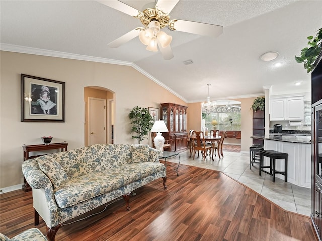 living room with ceiling fan, light wood-type flooring, lofted ceiling, a textured ceiling, and ornamental molding