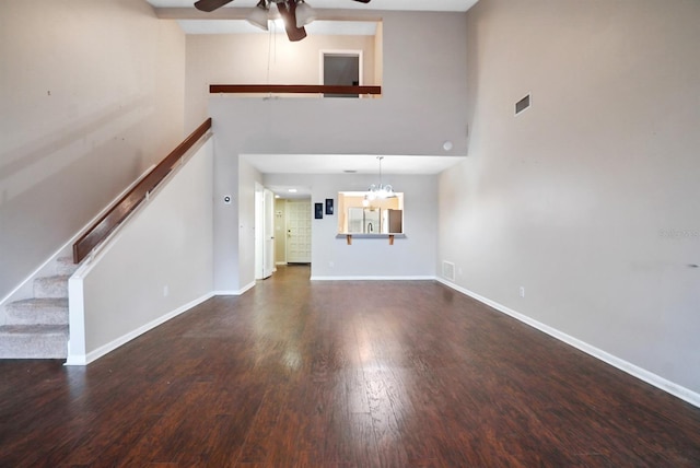 unfurnished living room featuring ceiling fan with notable chandelier, a towering ceiling, and dark wood-type flooring