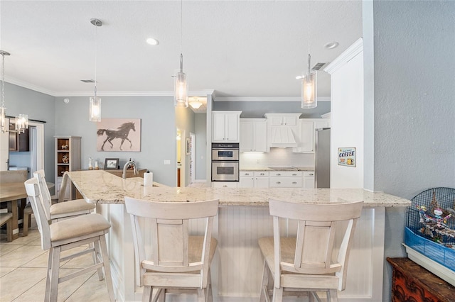 kitchen featuring appliances with stainless steel finishes, white cabinetry, pendant lighting, light stone counters, and a breakfast bar area