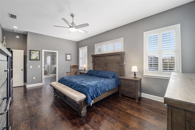 bedroom featuring ceiling fan, a tiled fireplace, dark hardwood / wood-style floors, and ensuite bath