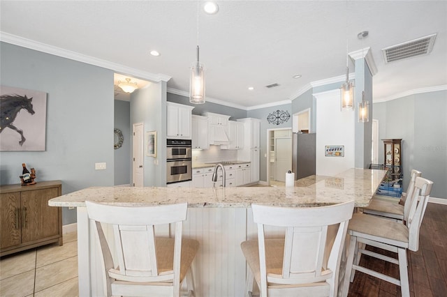 kitchen with pendant lighting, appliances with stainless steel finishes, white cabinetry, light stone counters, and a breakfast bar