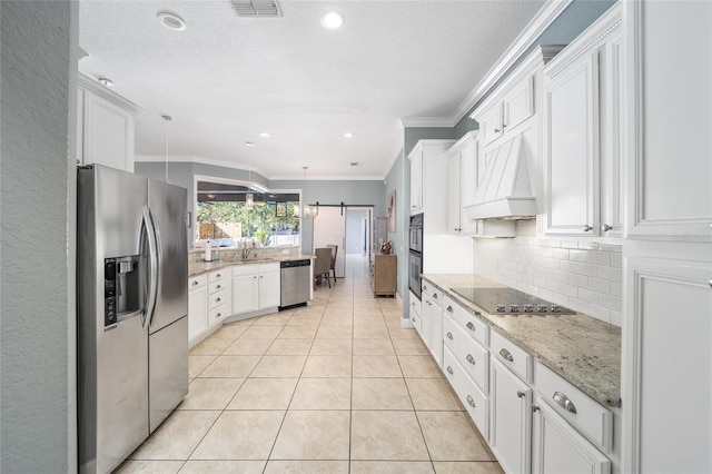 kitchen with white cabinets, appliances with stainless steel finishes, decorative light fixtures, premium range hood, and a barn door