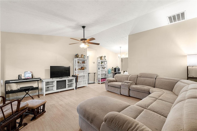 living room featuring ceiling fan with notable chandelier, light wood-type flooring, lofted ceiling, and a textured ceiling