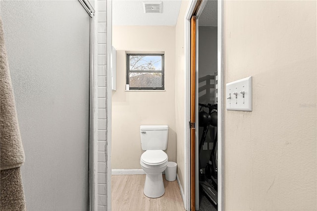 bathroom featuring a textured ceiling, wood-type flooring, a shower with shower door, and toilet