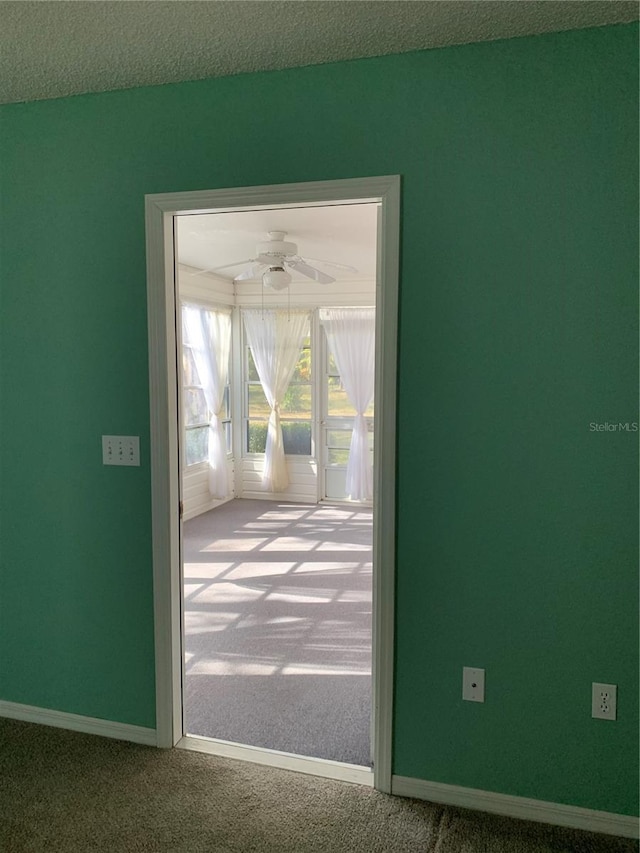 doorway with ceiling fan, carpet, and a textured ceiling