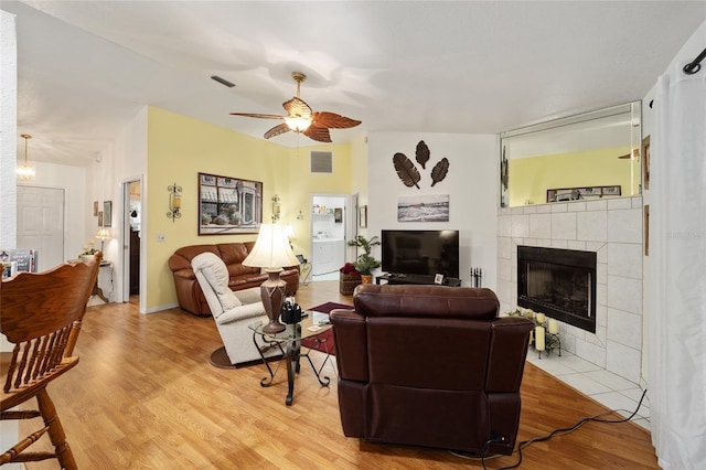 living room with a tiled fireplace, ceiling fan, and light wood-type flooring