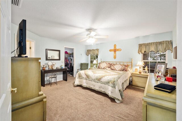 bedroom with a textured ceiling, a closet, carpet flooring, a walk in closet, and ceiling fan