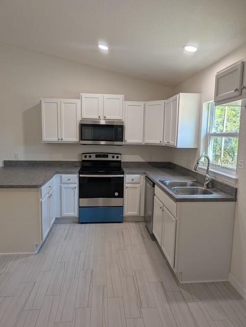 kitchen with appliances with stainless steel finishes, vaulted ceiling, white cabinetry, and sink