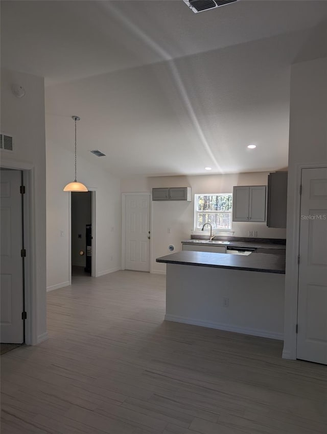 kitchen featuring gray cabinetry, lofted ceiling, sink, light wood-type flooring, and decorative light fixtures