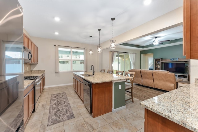 kitchen with light stone counters, sink, black appliances, pendant lighting, and a center island with sink