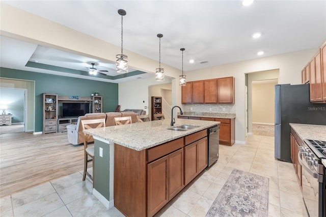 kitchen with ceiling fan, sink, stainless steel appliances, an island with sink, and decorative light fixtures