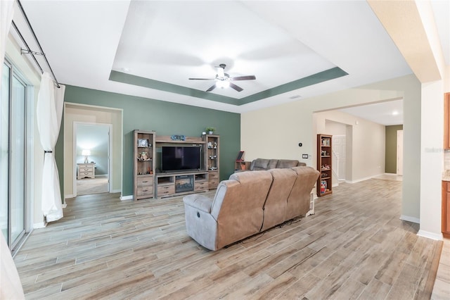 living room with ceiling fan, light wood-type flooring, and a tray ceiling