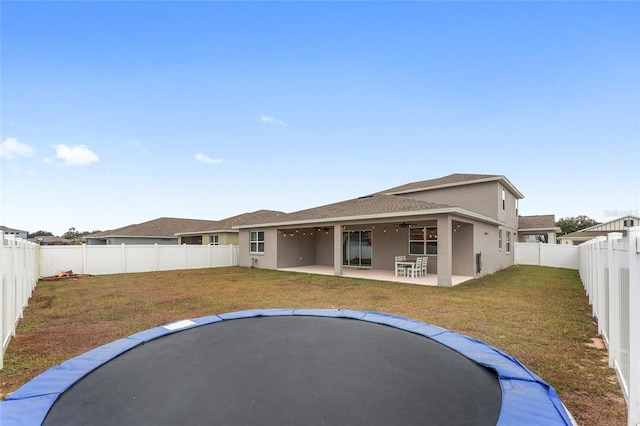 back of property featuring a yard, a patio, and a trampoline