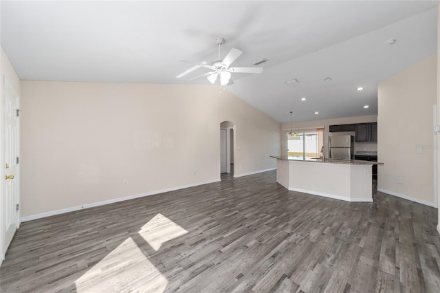 unfurnished living room with wood finished floors, baseboards, a ceiling fan, arched walkways, and vaulted ceiling