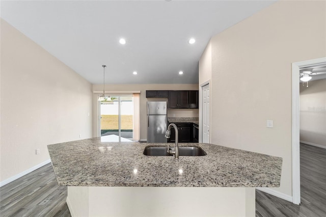 kitchen with a center island with sink, light stone counters, freestanding refrigerator, wood finished floors, and a sink