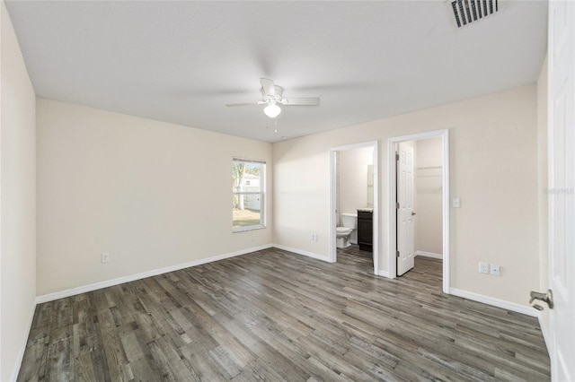 unfurnished bedroom with visible vents, baseboards, a walk in closet, and wood finished floors