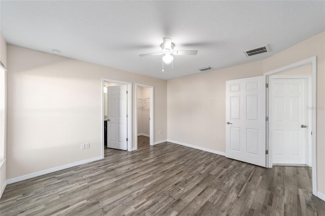 unfurnished bedroom with wood finished floors, visible vents, baseboards, a closet, and a walk in closet