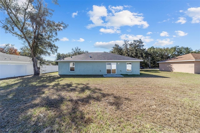 rear view of property featuring stucco siding, a yard, and fence