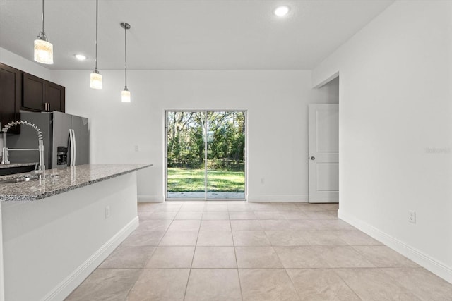 kitchen featuring pendant lighting, sink, light stone counters, light tile patterned floors, and dark brown cabinets