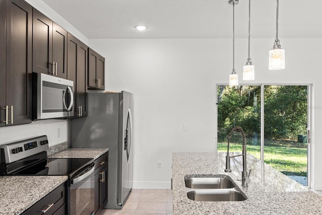 kitchen featuring stainless steel appliances, sink, hanging light fixtures, light stone counters, and dark brown cabinets