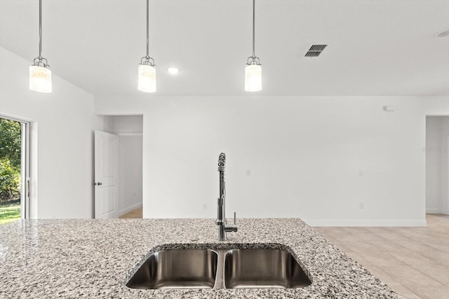 kitchen featuring hanging light fixtures, sink, and light stone counters