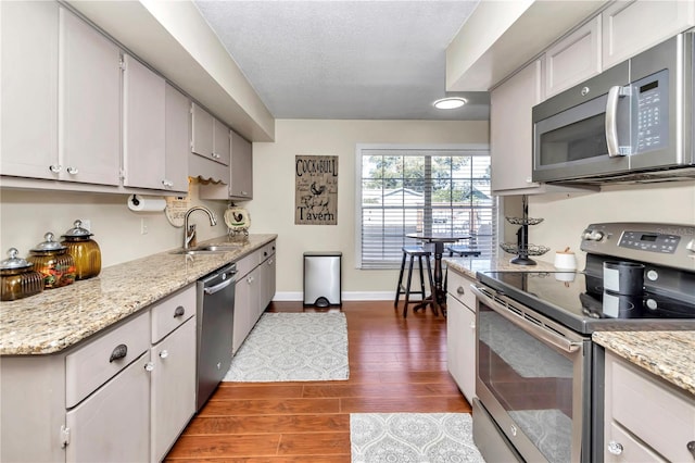 kitchen featuring sink, a textured ceiling, appliances with stainless steel finishes, dark hardwood / wood-style flooring, and light stone counters