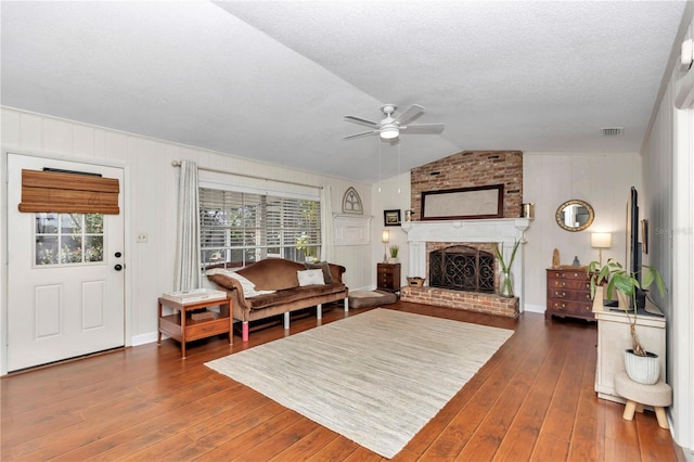 living room featuring vaulted ceiling, a brick fireplace, ceiling fan, and dark wood-type flooring