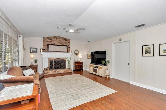 living room featuring dark hardwood / wood-style flooring, a brick fireplace, a textured ceiling, vaulted ceiling, and ceiling fan