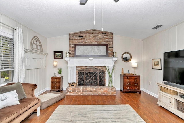 living room featuring a fireplace, a textured ceiling, hardwood / wood-style flooring, and vaulted ceiling