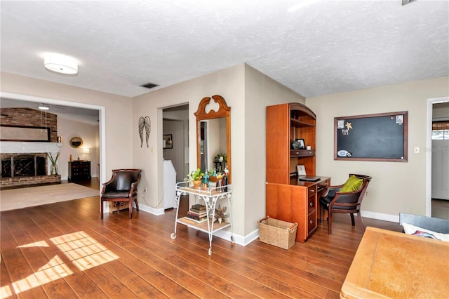 living room with hardwood / wood-style floors, a textured ceiling, and a brick fireplace