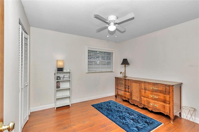 living area with ceiling fan, a textured ceiling, and hardwood / wood-style flooring