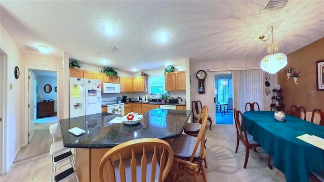 kitchen with white appliances, a textured ceiling, a chandelier, a center island, and decorative light fixtures