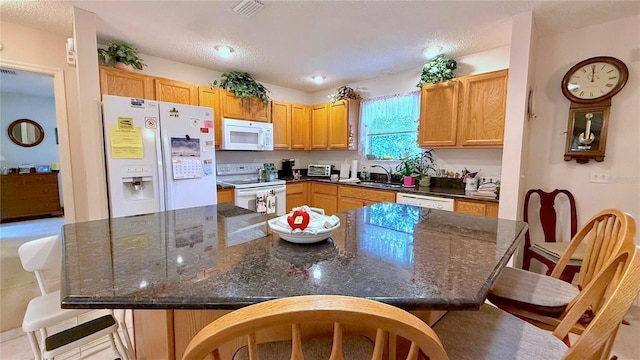 kitchen featuring white appliances, dark stone countertops, a kitchen island, and sink